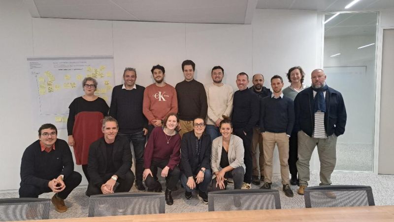 L'image montre 15 personnes posant devant un bureau. Ils sourient