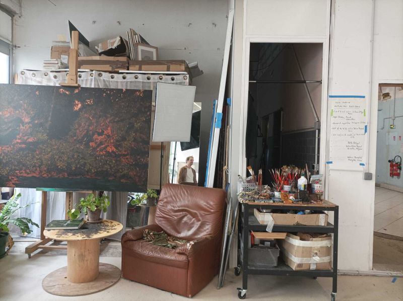 L'image montre un intérieur d'atelier d'artistes avec des peintures, un fauteuil, un miroir