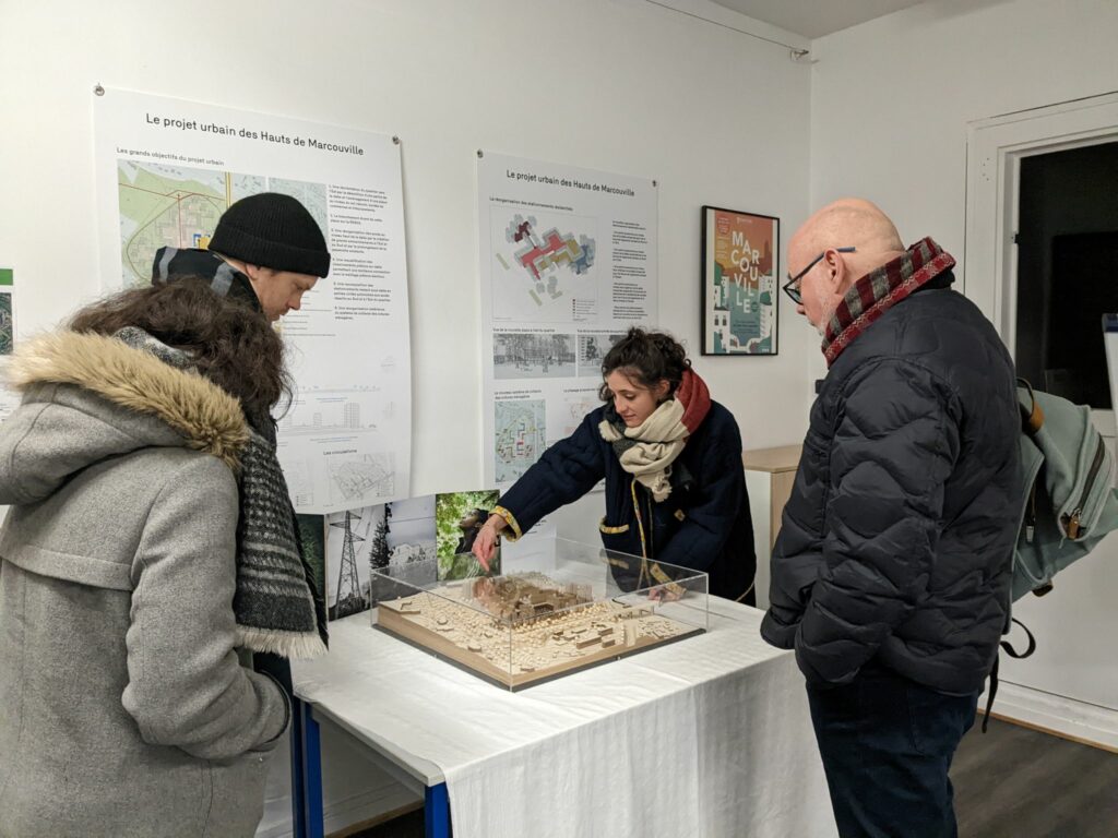 L'image montre 3 personnes en intérieur autour d'une maquette du quartier