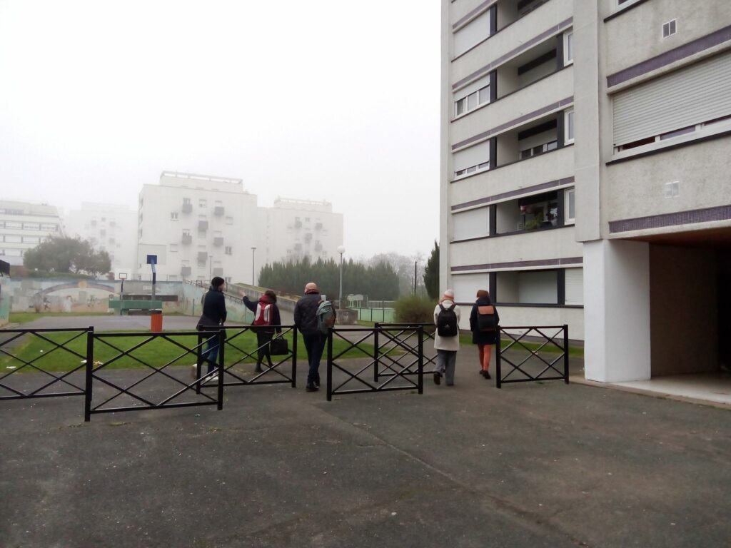 L'image montre 4 personnes marchant sur un parvis de tours, dans le brouillard.